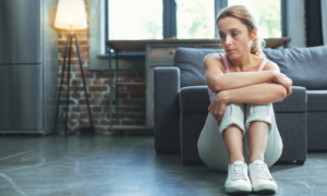 A woman sitting on the floor with her back against the wall, looking down, embodying sadness and contemplation